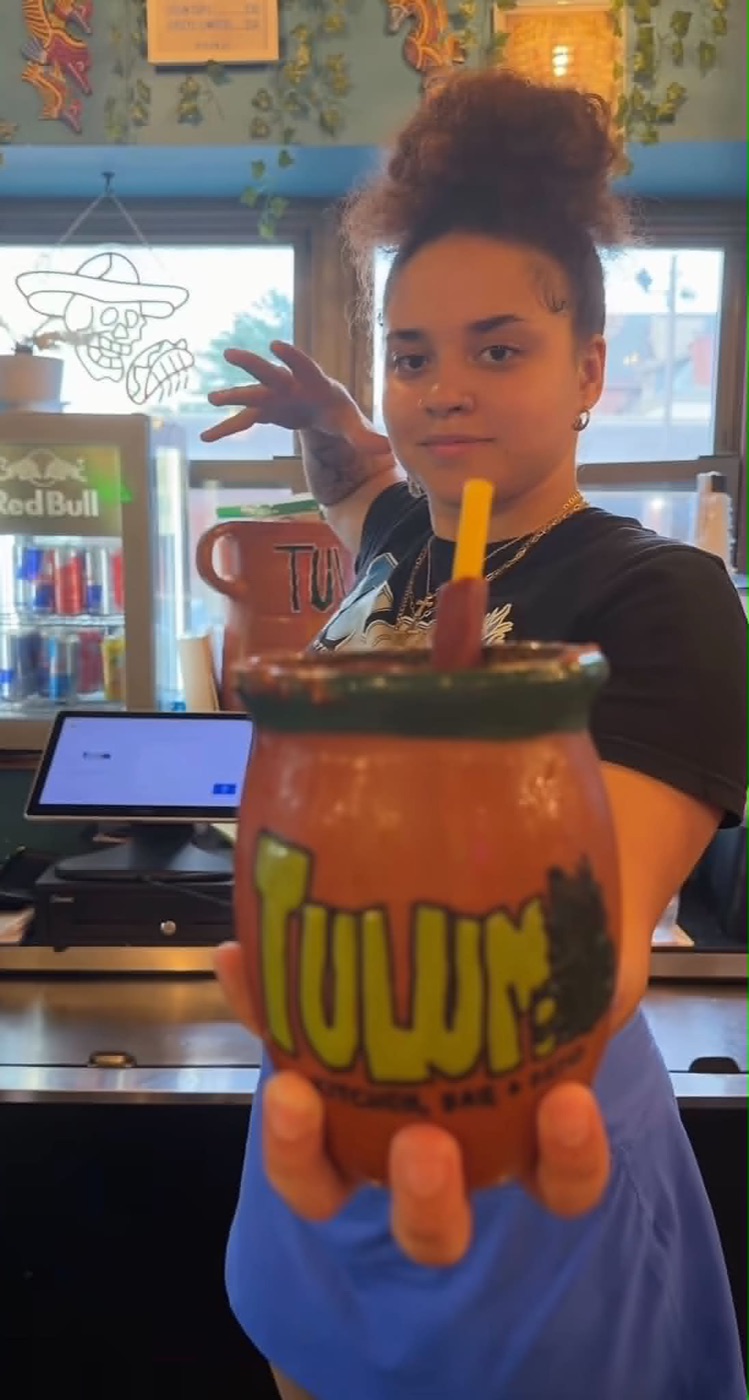 A Tulum team member behind the bar holding a house margarita in a hand-painted clay mug